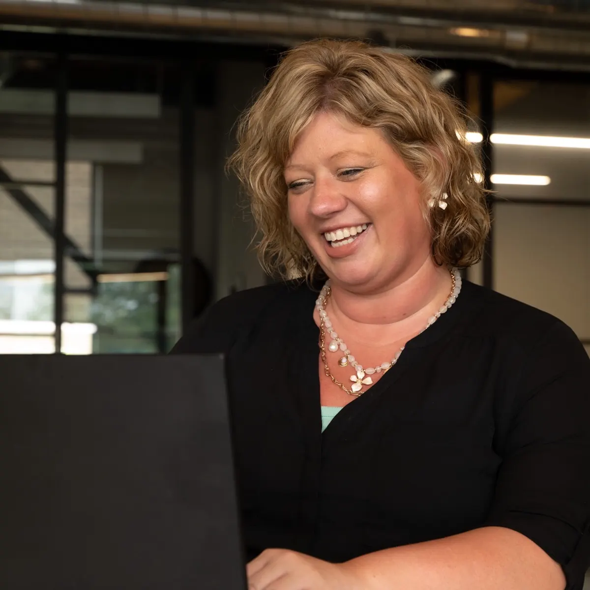 A Sympl Benefits team member smiling at her laptop in the Sympl office near Grand Rapids, Michigan