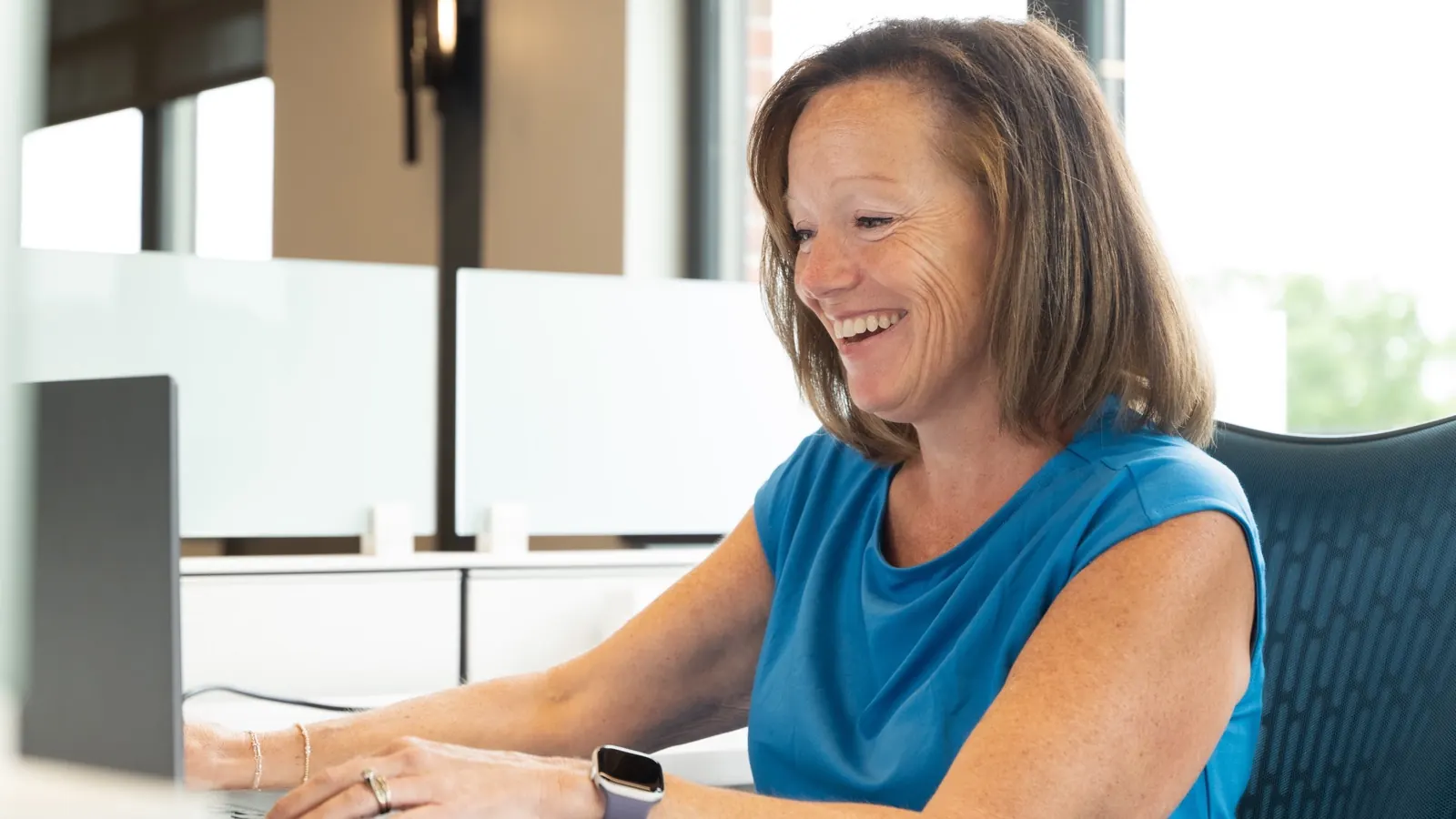 A Sympl Benefits team member smiling at her laptop in the Ada, Michigan office